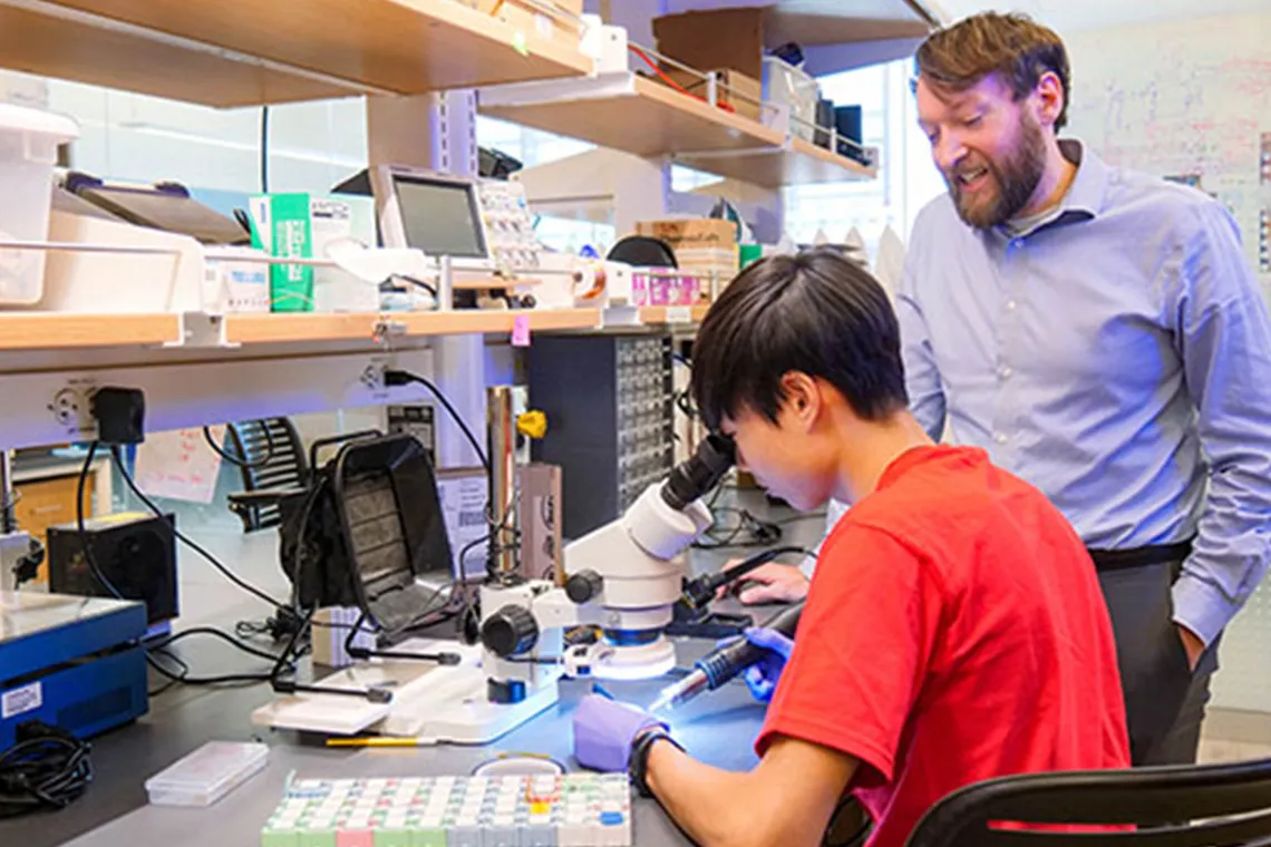 a student using a microscope with a scientist next to them