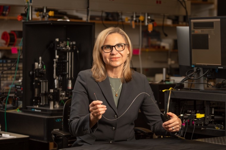 Dr. Jennifer Barton in her lab wearing a dark gray suit jacket and dark glasses holding wire imaging device