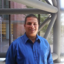 Robert Sandoval wearing a blue shirt against a gray geometric background